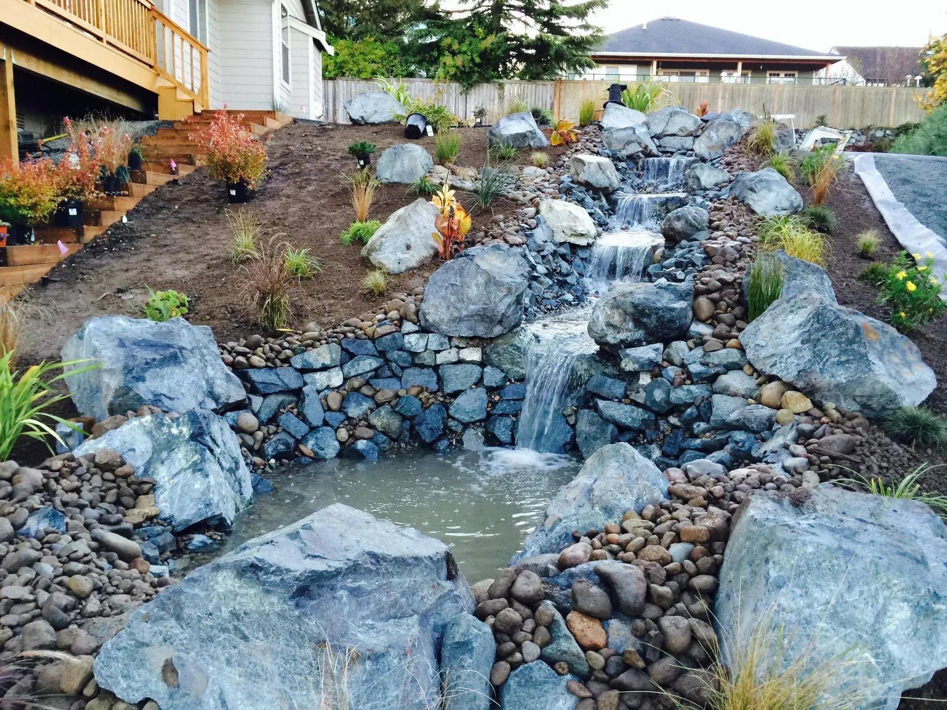 Water cascading down a rocky waterfall into a small pond, landscaping in a yard.