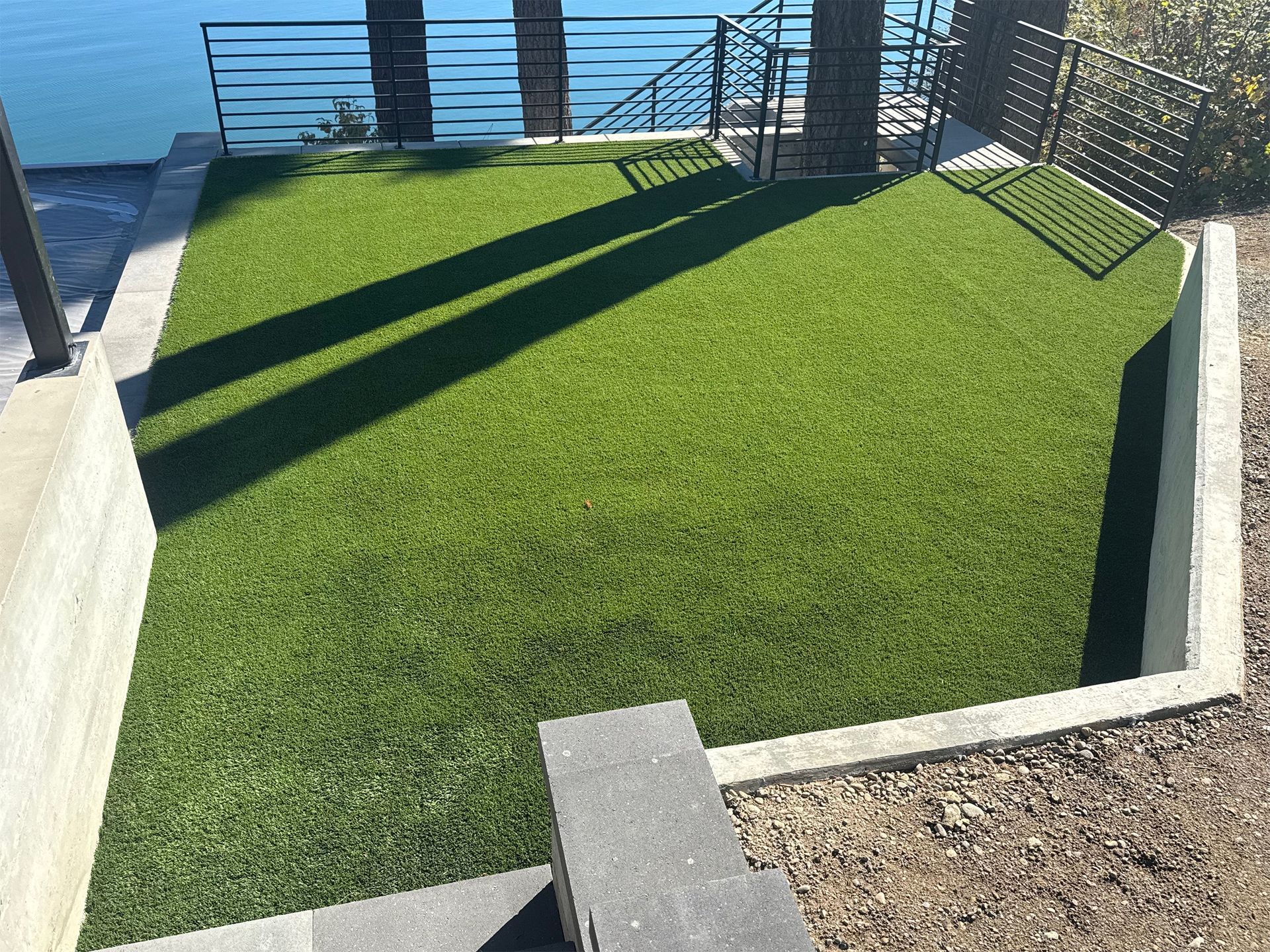 Green artificial turf in a sunken area with concrete borders, near water and railings.