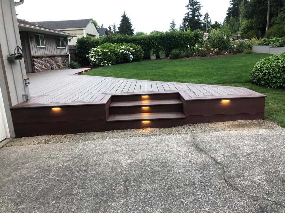 Composite deck with steps, built-in lights, and a yard beyond. Brown deck and stairs, beige house in background.
