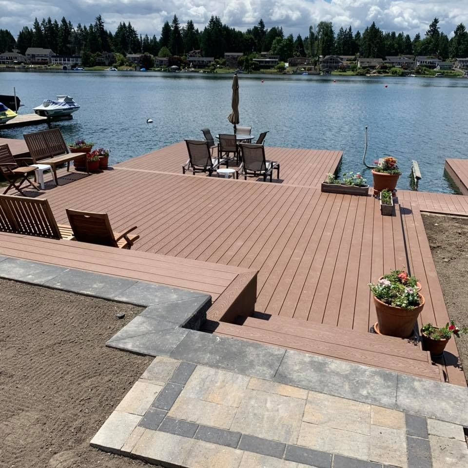 A wooden dock with patio furniture on a lake. Steps lead to the deck.