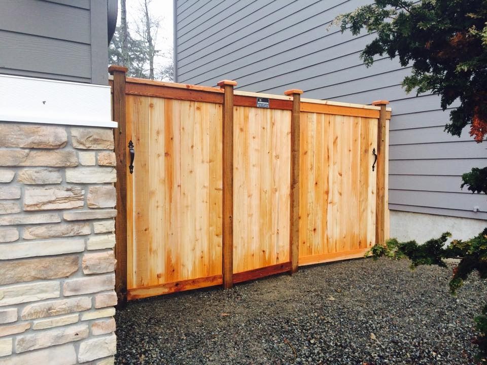Wooden gate in a gravel yard, next to a stone wall and a gray house.