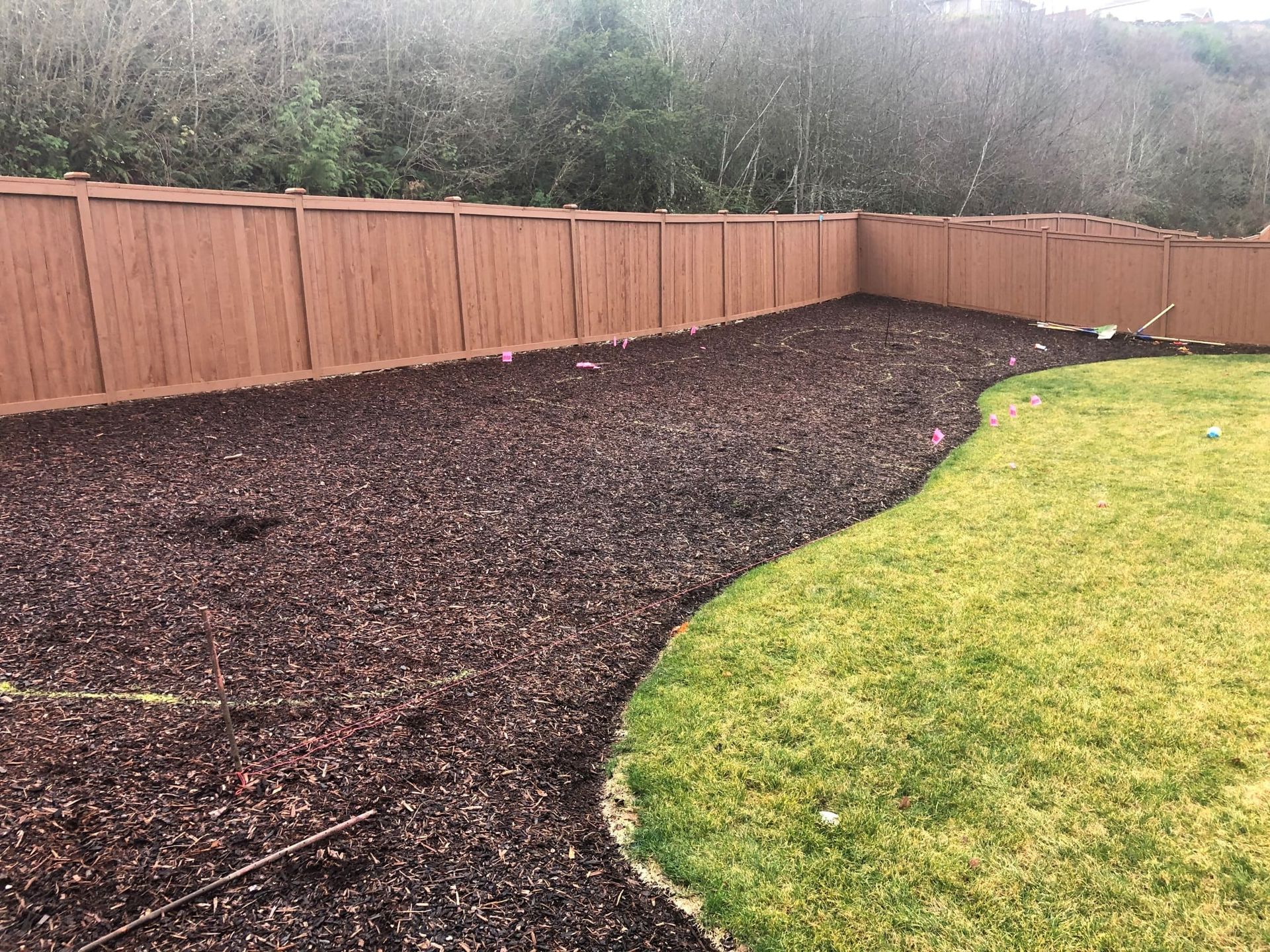 Brown mulch bed along a brown fence and green grass.