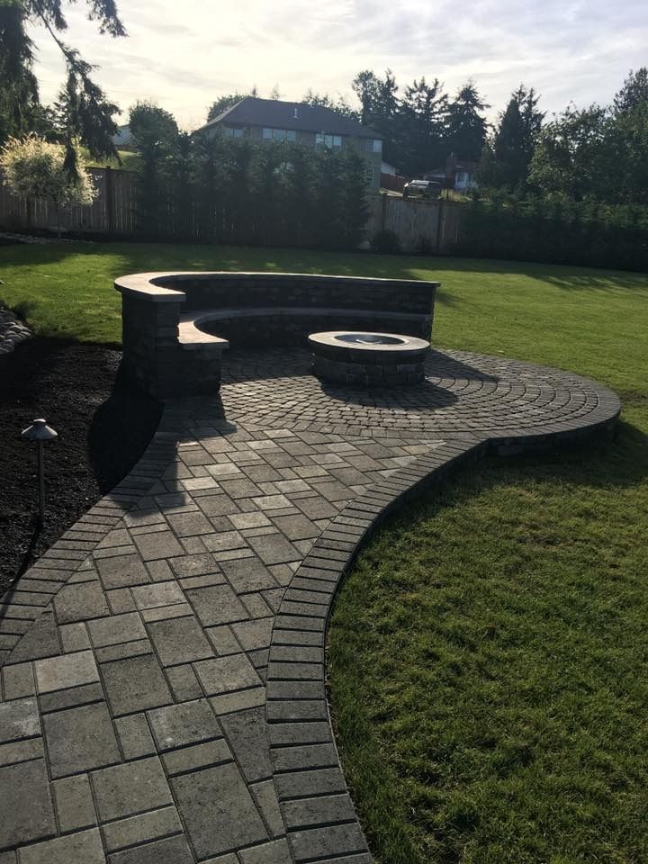 Brick patio with fire pit and curved bench in grassy yard.