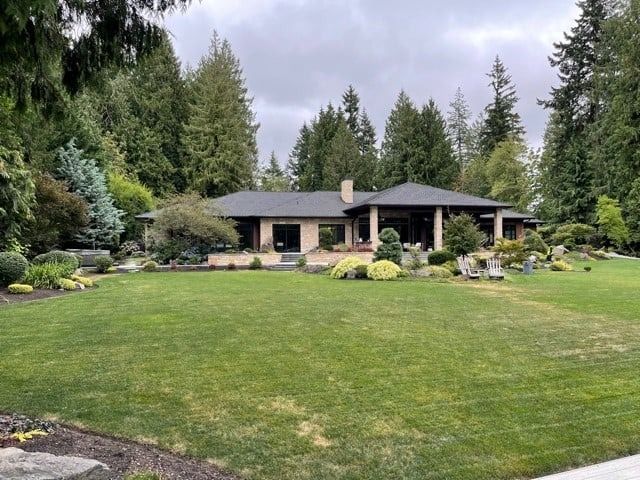 A large, single-story house with a green lawn and surrounding trees under a cloudy sky.