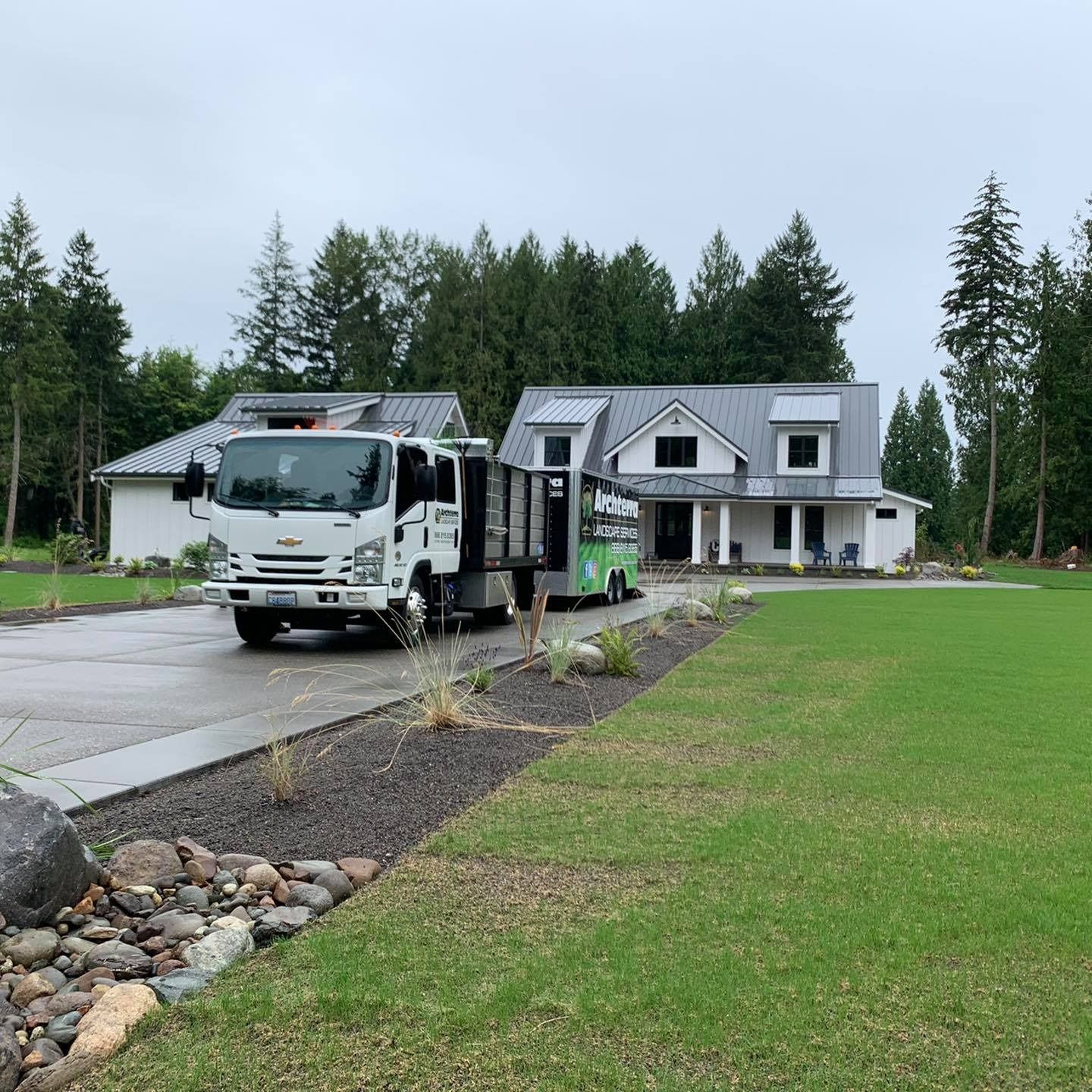 A white truck and trailer parked in front of a modern house on a grassy lot.