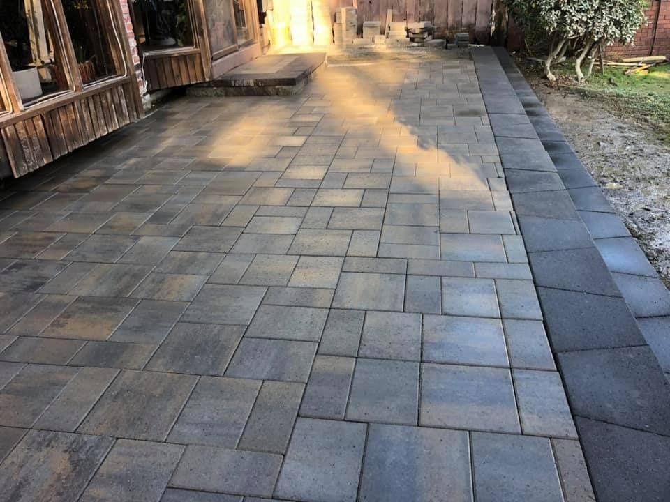 Brick patio with varying shades of gray paving stones, leading to steps near a wooden structure.