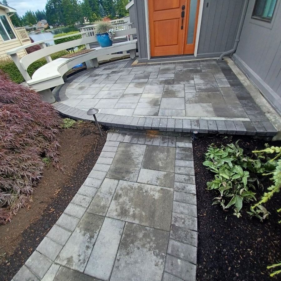 Gray paver patio and walkway leading to an orange door. A Japanese maple and shrubs flank the entrance.