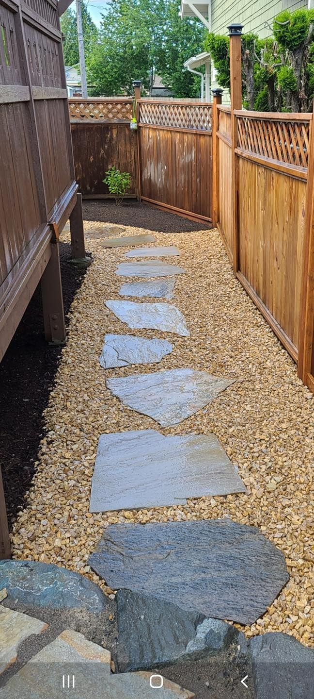 Stone path through a gravel bed, bordered by wooden fences and a deck.