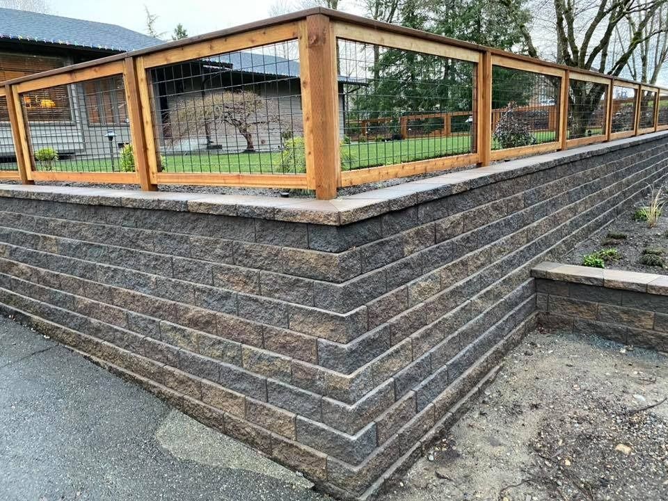Brown retaining wall topped with a wooden fence and wire mesh, outdoors.