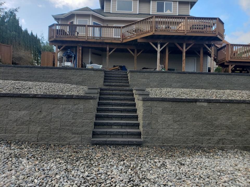 Stone retaining walls and stairs leading up to a house with a large deck.