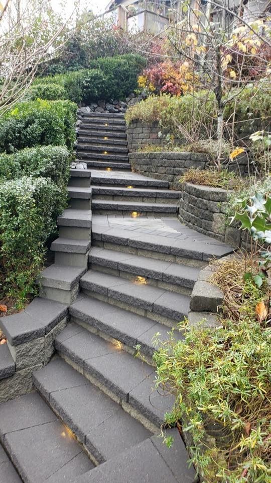 Stone staircase ascending a hillside with landscaping, lit by built-in lights.