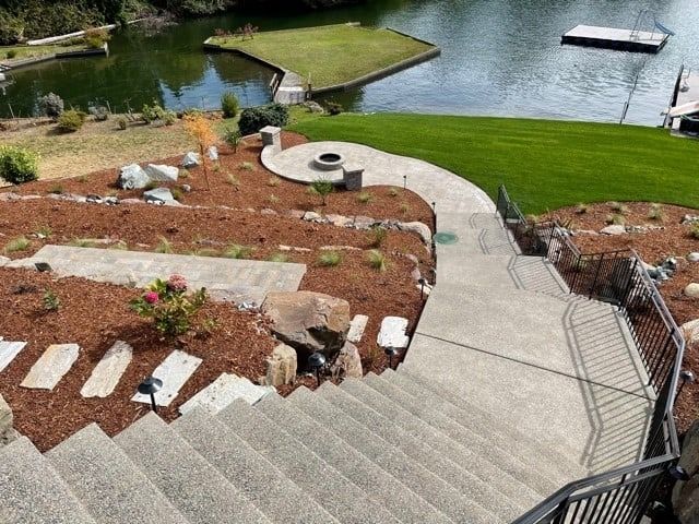 Stone stairs leading to a landscaped area with a lake, fire pit, and green grass.