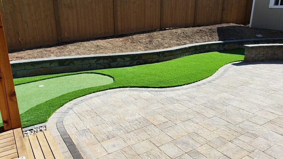 Backyard patio with putting green bordered by stone and wooden fence.