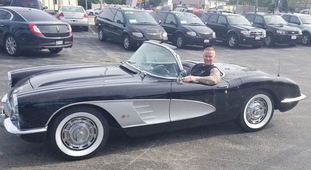 Man sitting in a black-and-silver classic convertible car in a parking lot
