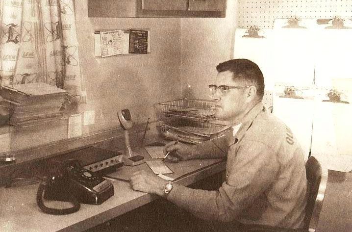 A black and white photo of a man sitting at a desk.