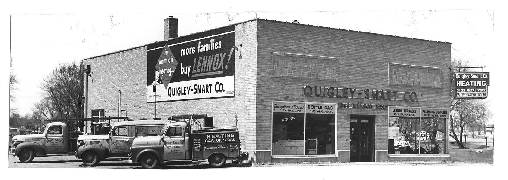 A black and white photo of a building with trucks parked in front of it.