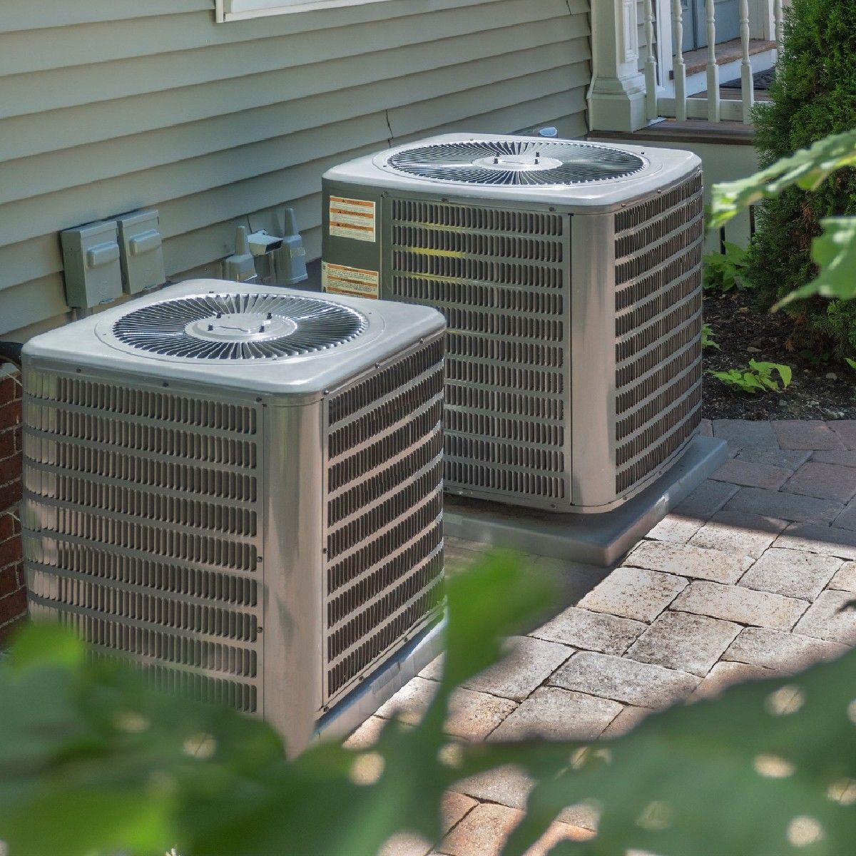 Two air conditioners are sitting on the side of a house.