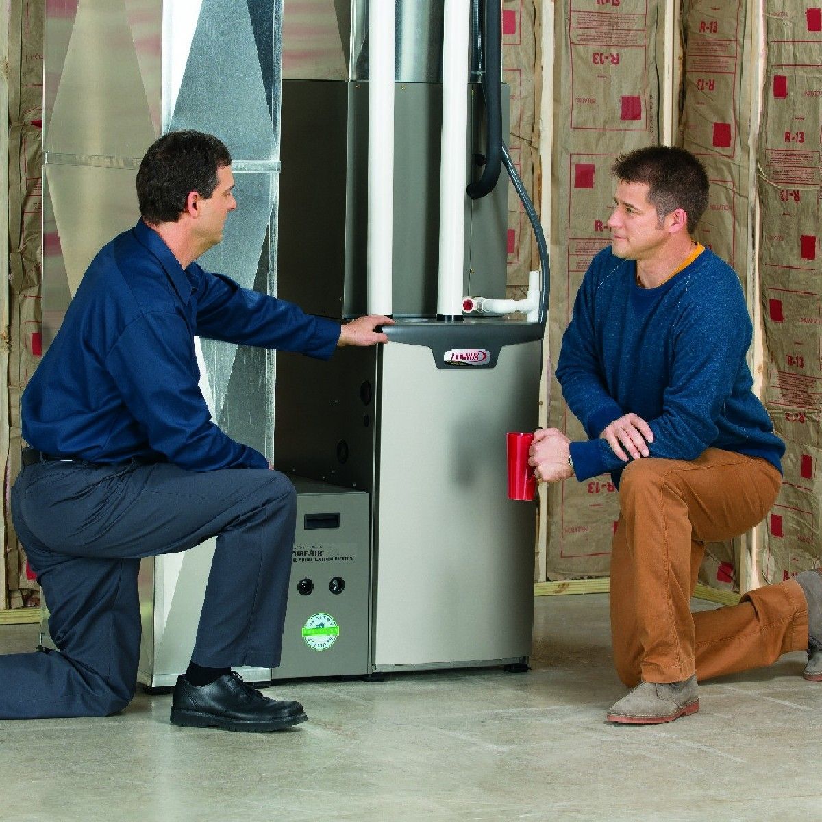 Two men are kneeling in front of a lennox heater.