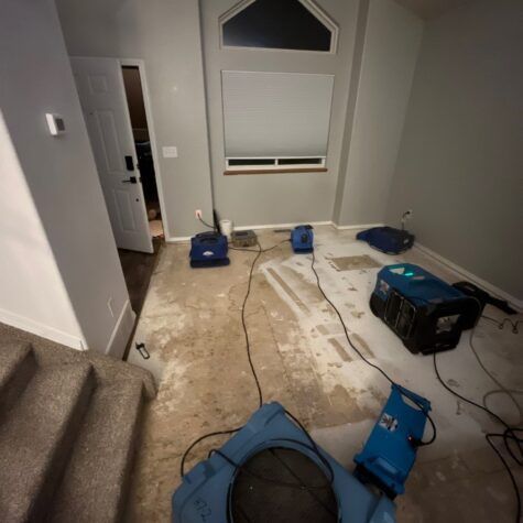 Messy room with wet floor and cleaning/drying equipment, likely from water damage near a window.