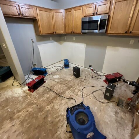 Kitchen with water-damaged floor, drying machines, and exposed cabinets after cleanup work