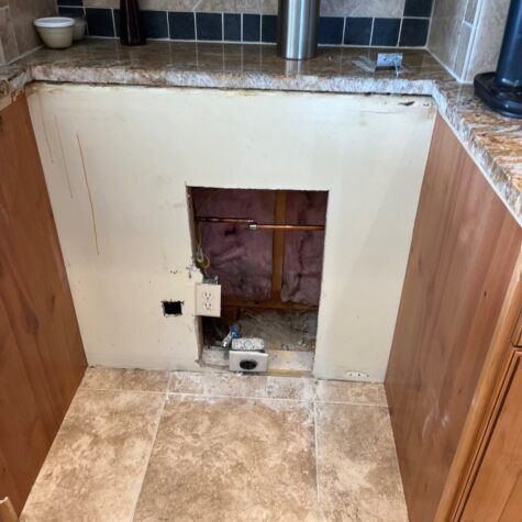 Kitchen cabinet base with an open cutout exposing plumbing and wiring under the counter