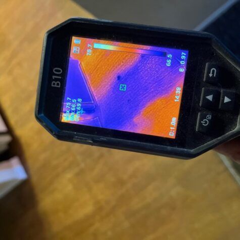 Handheld thermal camera showing a colorful heat map with orange and purple areas on its screen