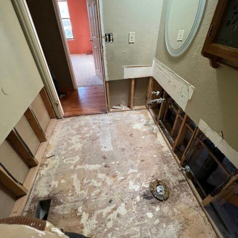 Bathroom under renovation with exposed wall studs, removed flooring, and debris on the floor.
