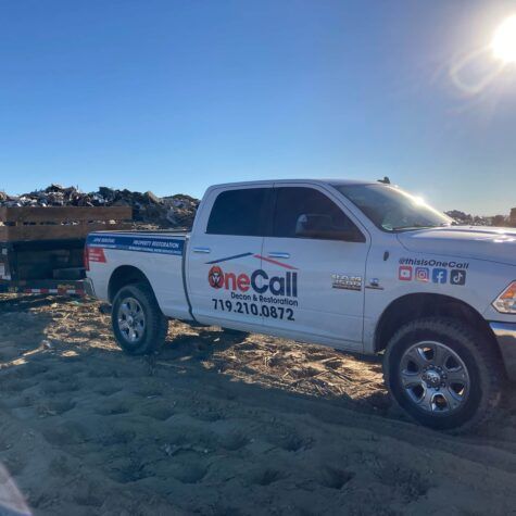 White OneCall service pickup truck parked on a sandy beach under a bright sun.