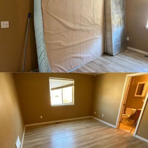 Empty tan bedroom with light wood floors, a window, and a doorway to a bathroom.