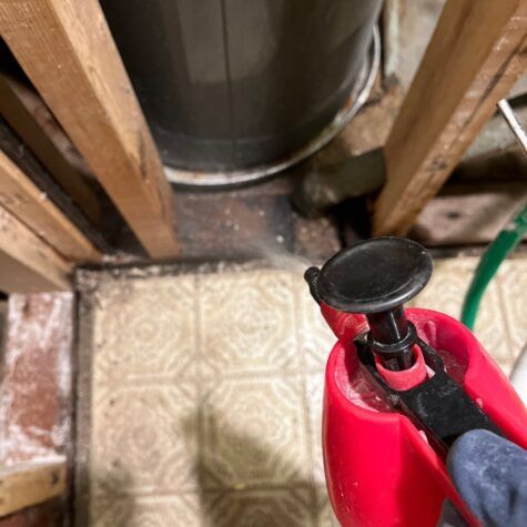 A red pipe wrench held near plumbing pipes under a sink in a utility area