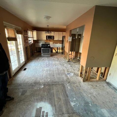 Damaged kitchen and dining room with torn-out flooring and exposed wall studs