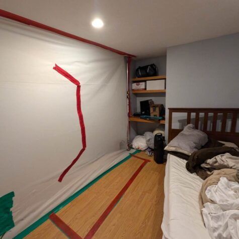 A bedroom with a bed, shelves, and a large white sheet taped to the wall with red tape lines.
