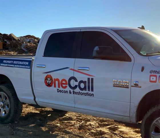 White One Call Decon & Restoration pickup truck parked on a rocky shoreline under a clear sky