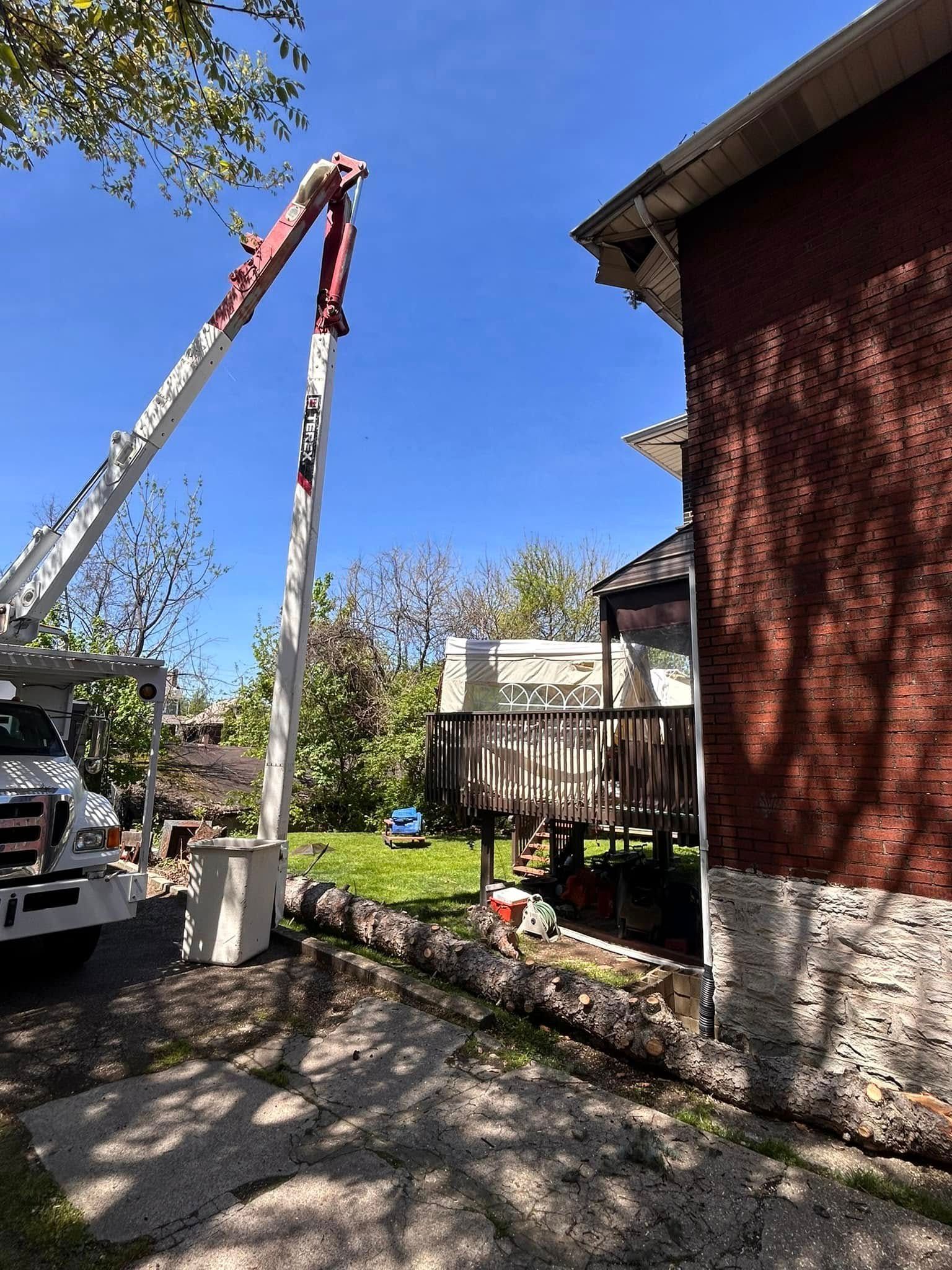 Tree trimming truck with boom lift beside a red brick house in a sunny yard