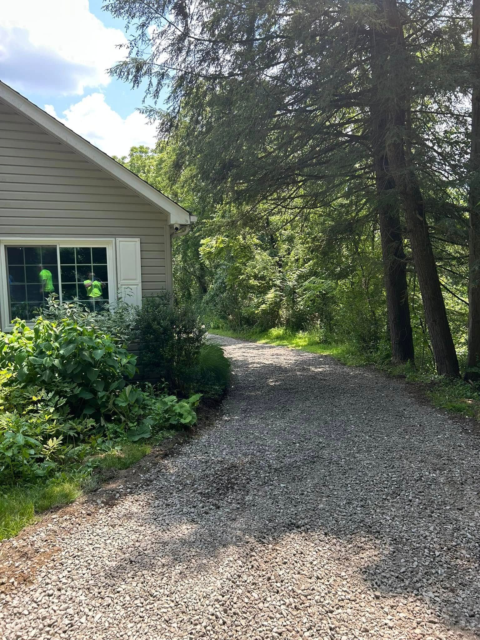 Gravel driveway beside a house, lined with trees and sunlit greenery