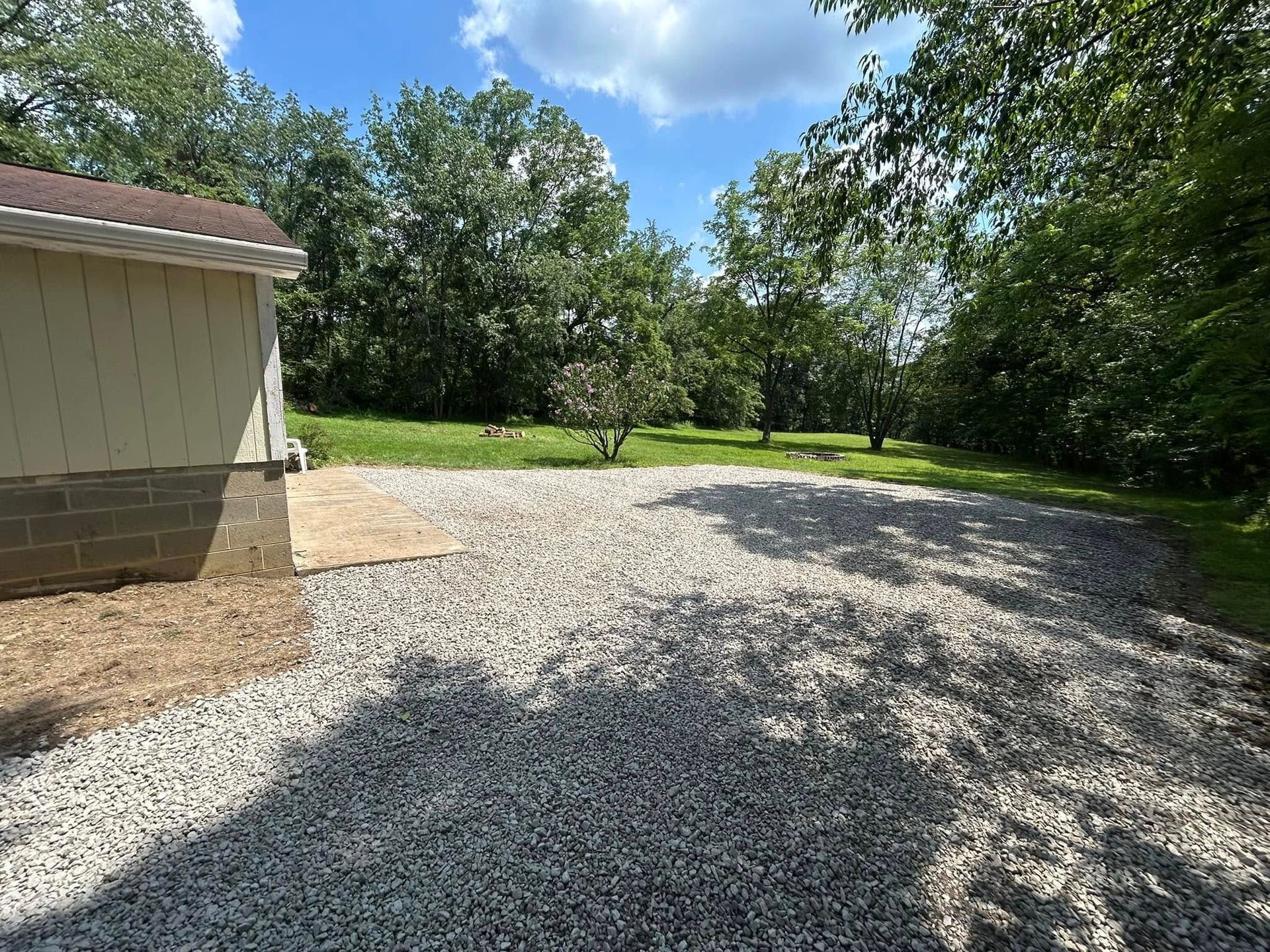 Gravel driveway beside a beige building, with green trees and grass under a blue sky.