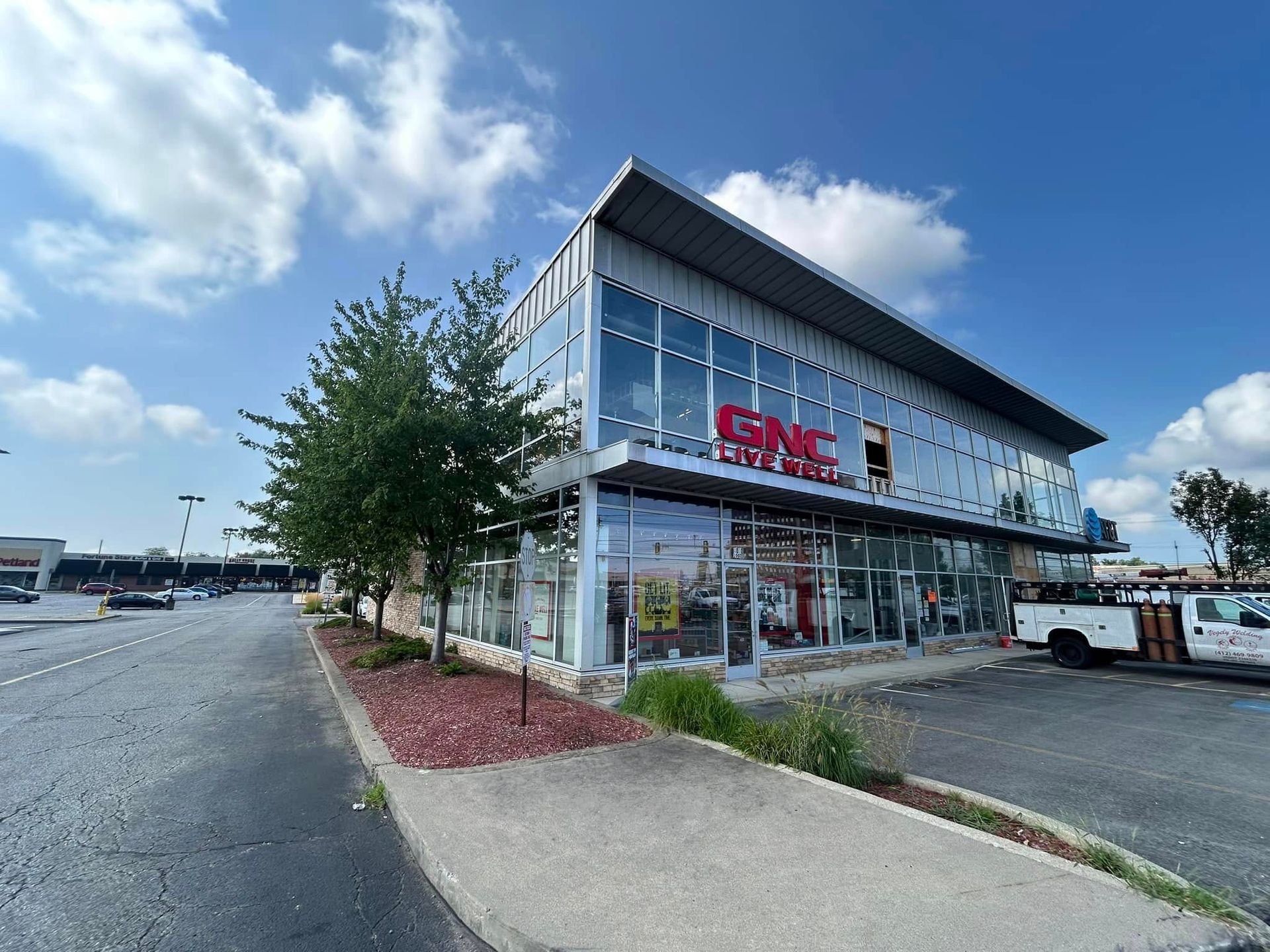 Modern glass storefront with red signage beside a parking lot on a cloudy day