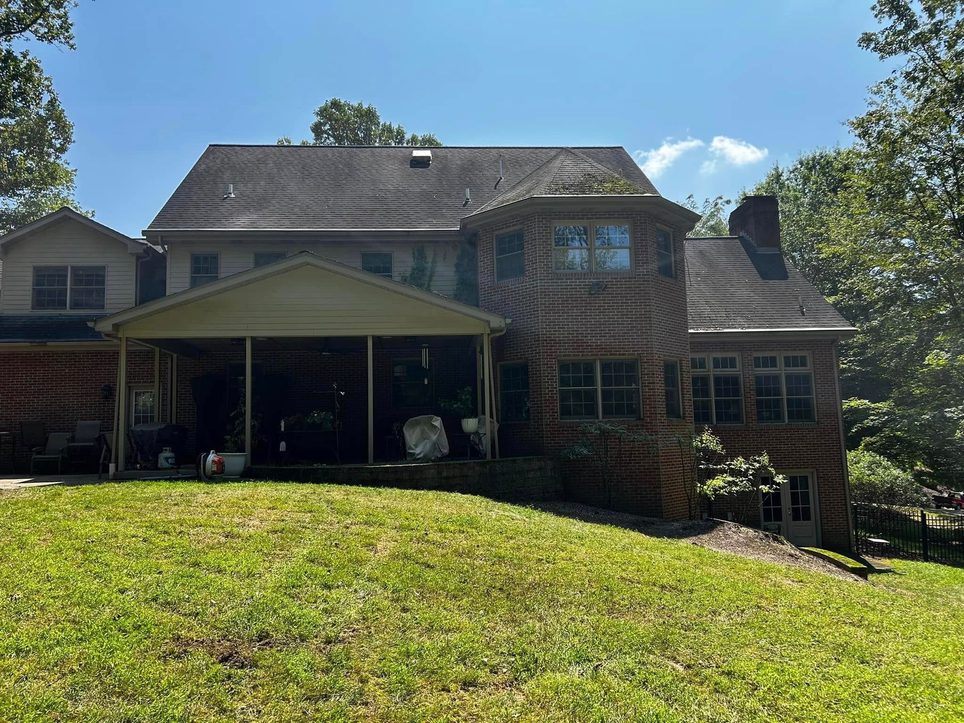 Brick two-story house with a covered front porch and large grassy sloped yard in sunlight