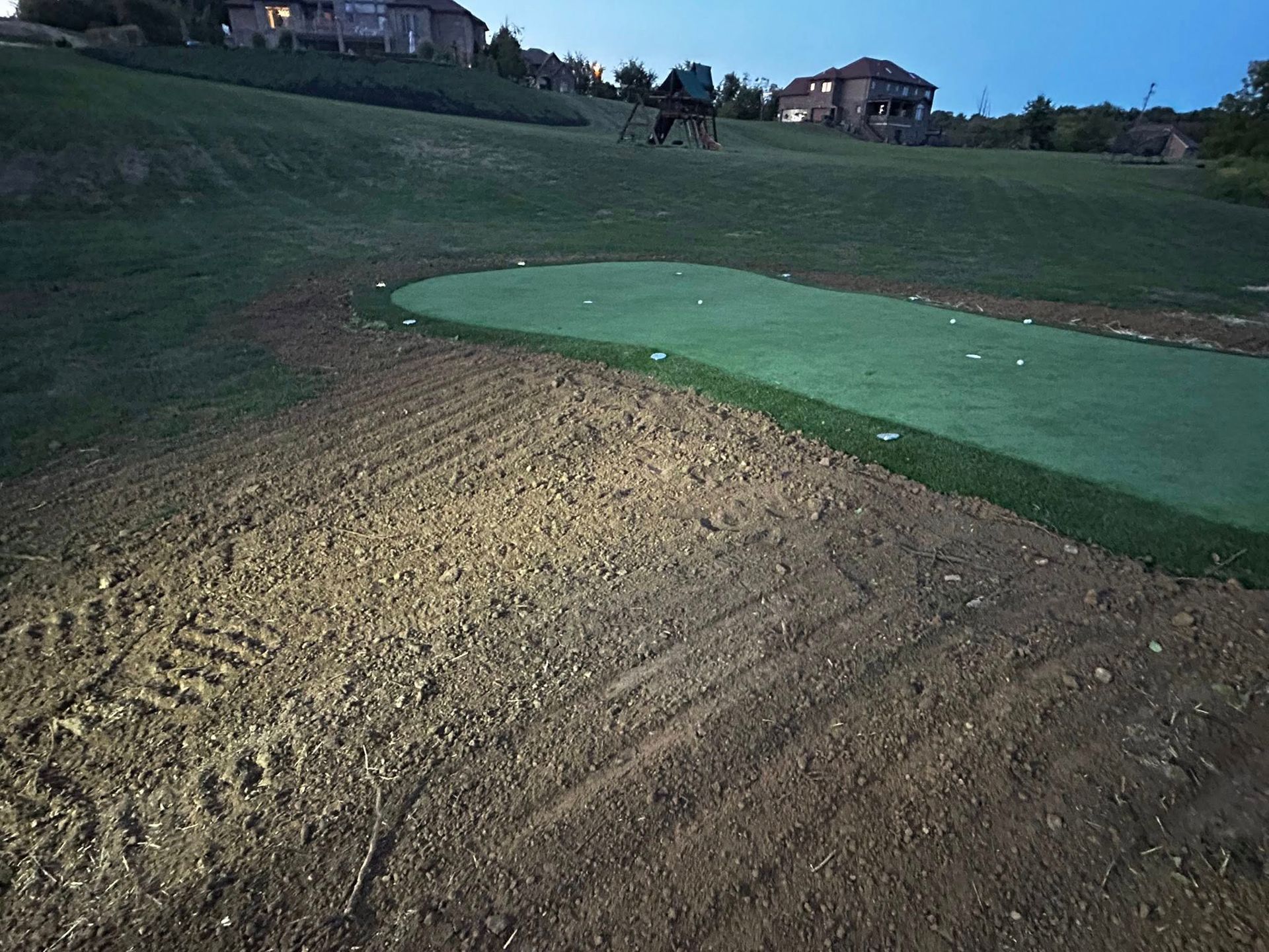 Golf course bunker beside a green at dusk, with a golfer in the distance.