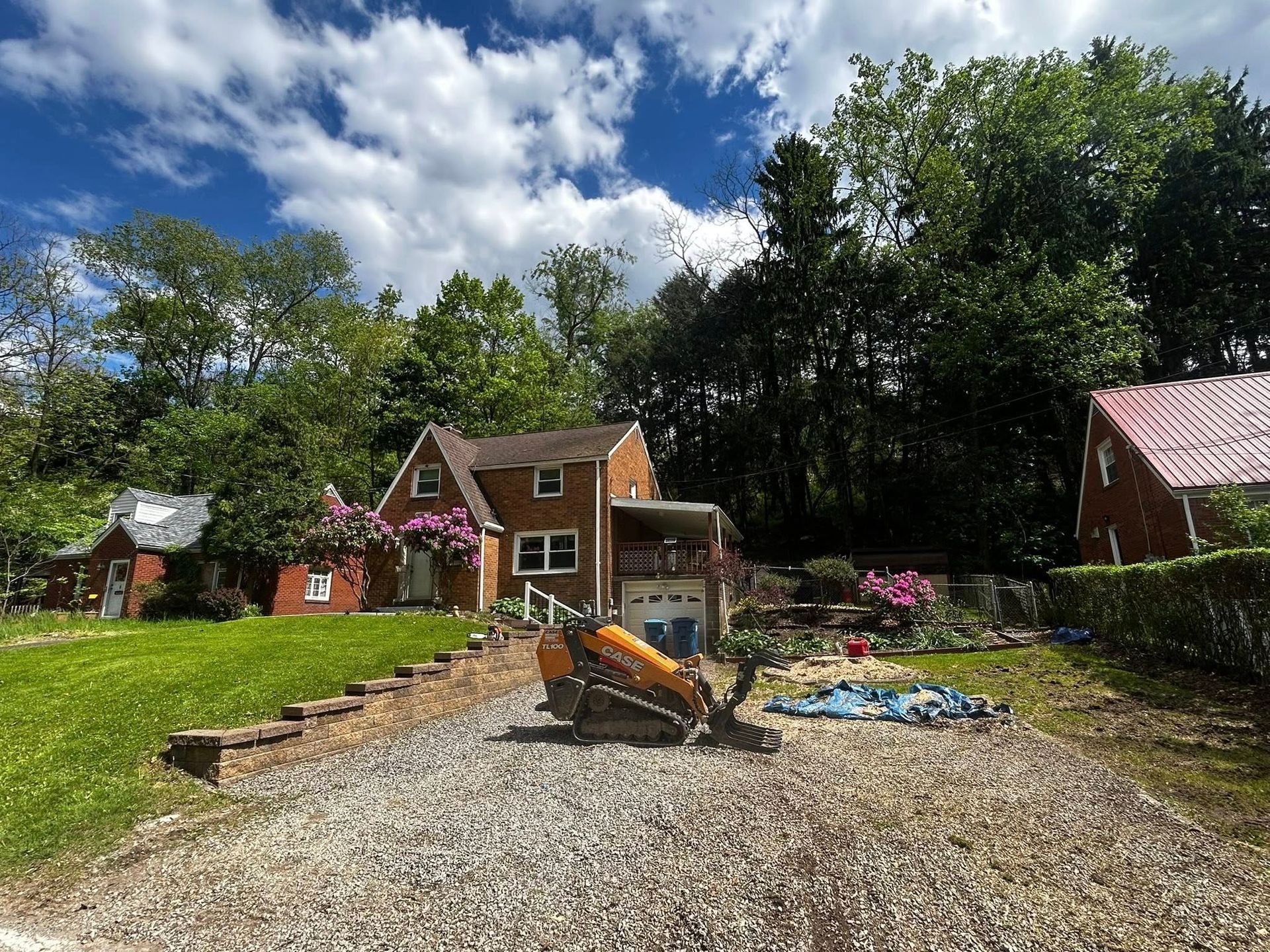 Gravel play area with a slide, playground equipment, and a small house under a partly cloudy sky.