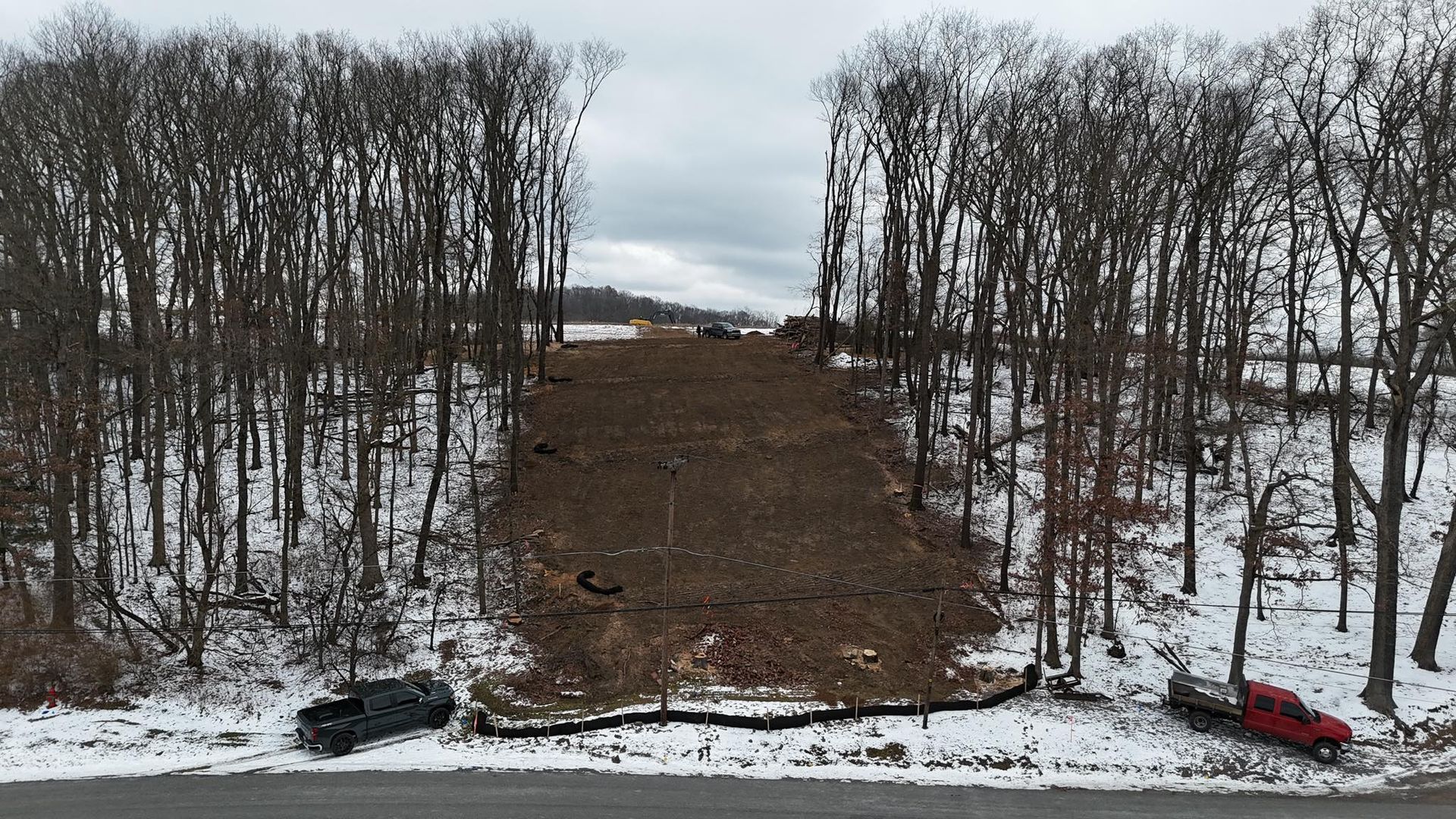 Snow-covered hillside with a cleared brown path through bare trees and a red car at the bottom right.
