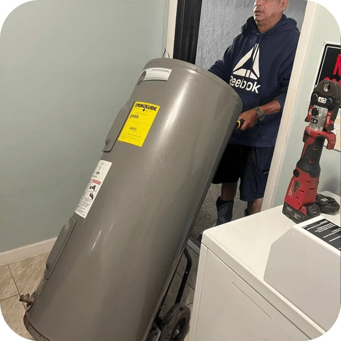 Man moving a water heater on a dolly in a utility room.