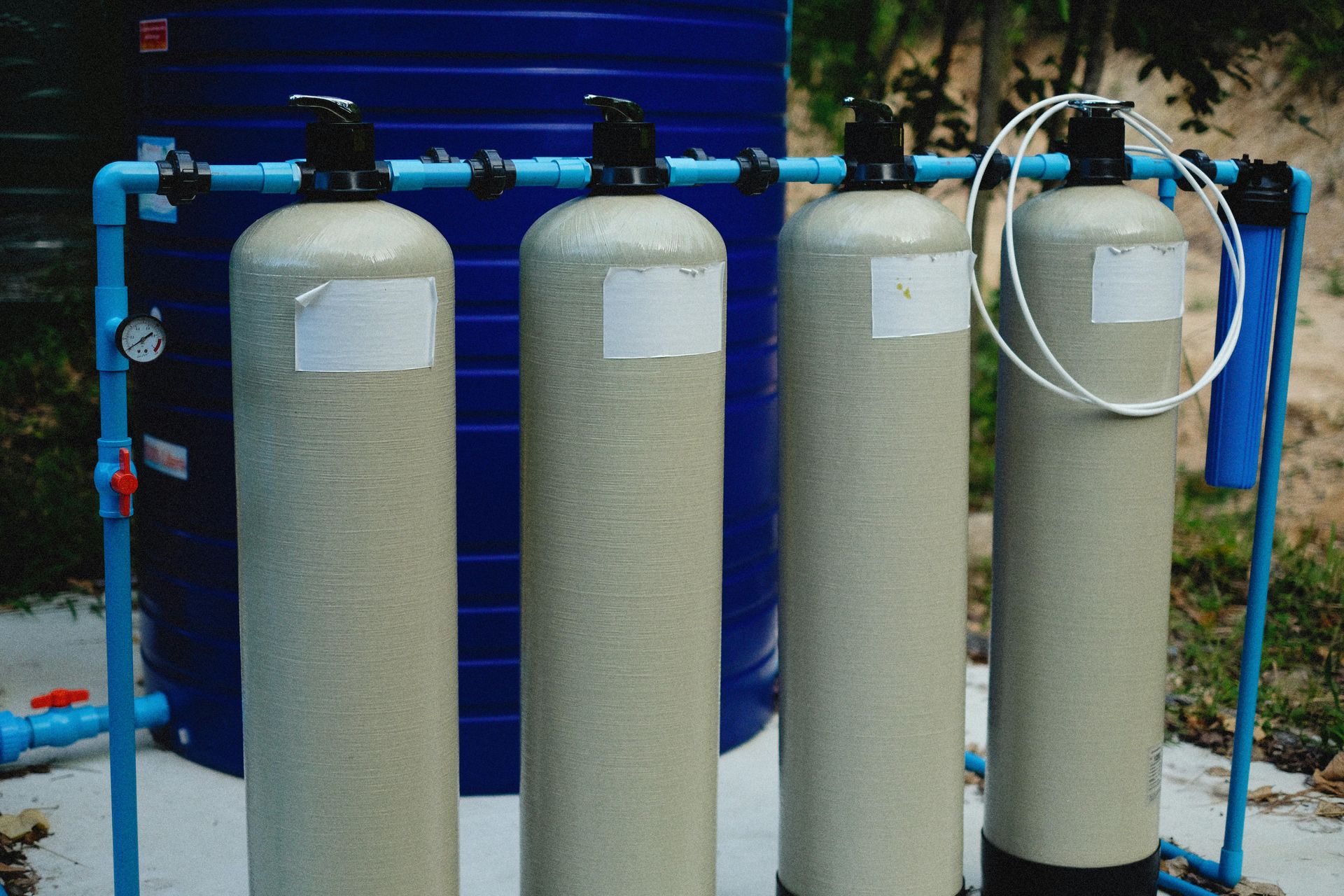 Water filtration system: four beige cylindrical tanks, blue pipes, and a blue water tank in the background.