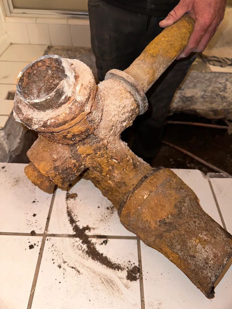 Rusty, corroded plumbing fixture held by a person indoors, on tiled floor.