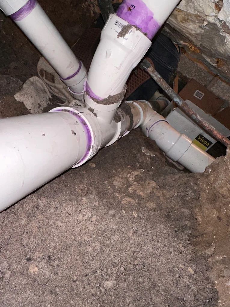 PVC plumbing pipes joined together, showing purple primer at the joints in an excavated area.