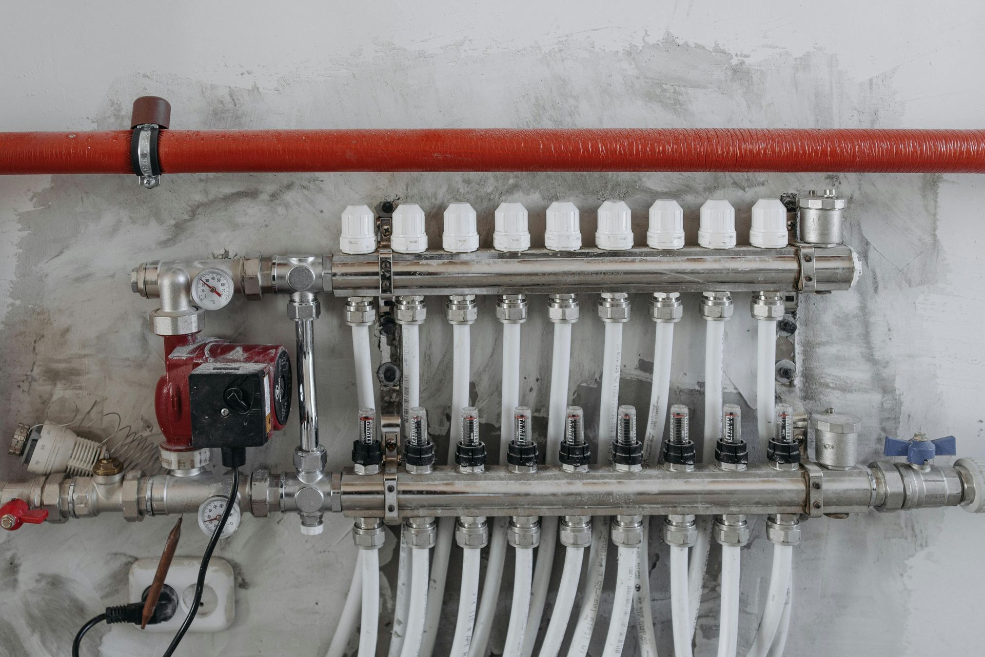 Piping system with red pump, connected to white and silver pipes, mounted on a concrete wall.