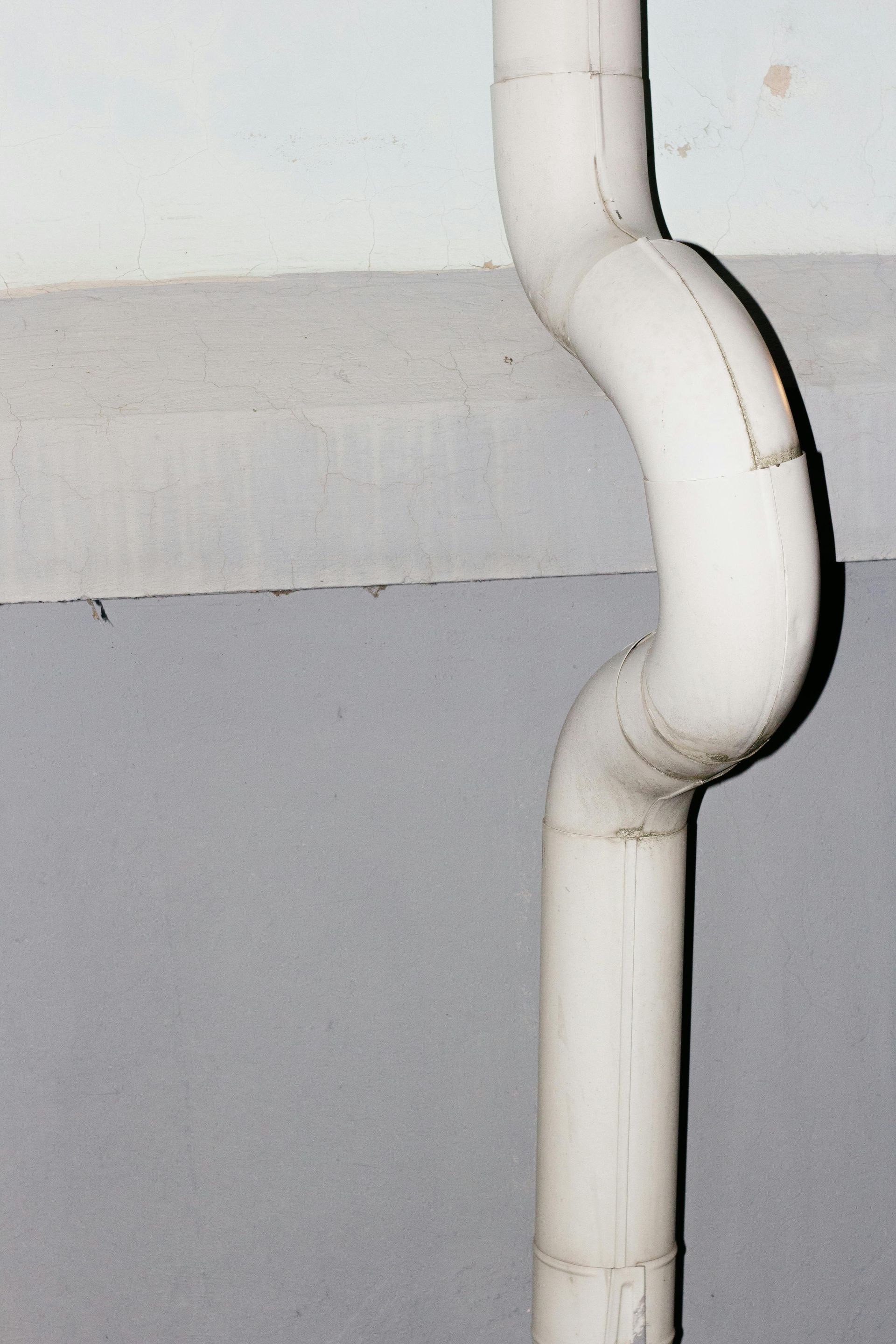 White, curved downspout against gray and light gray walls.