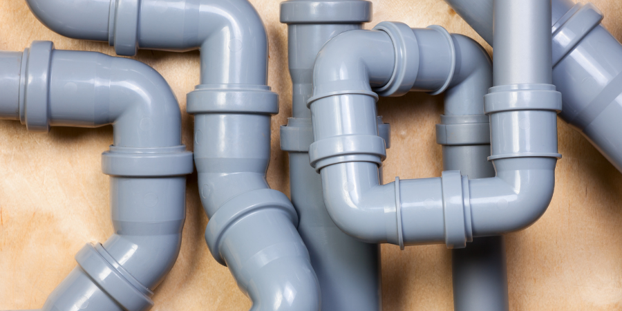 Gray plastic plumbing pipes against a tan wall, various shapes and orientations.