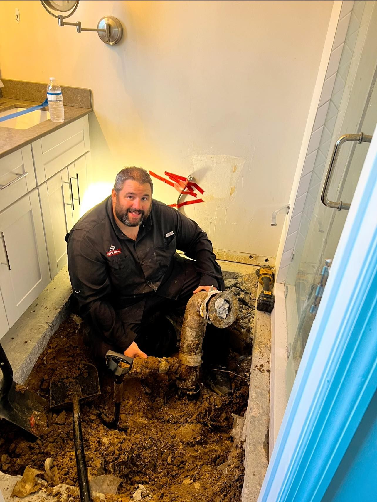 Plumber working on pipes in bathroom, surrounded by dirt and tools.