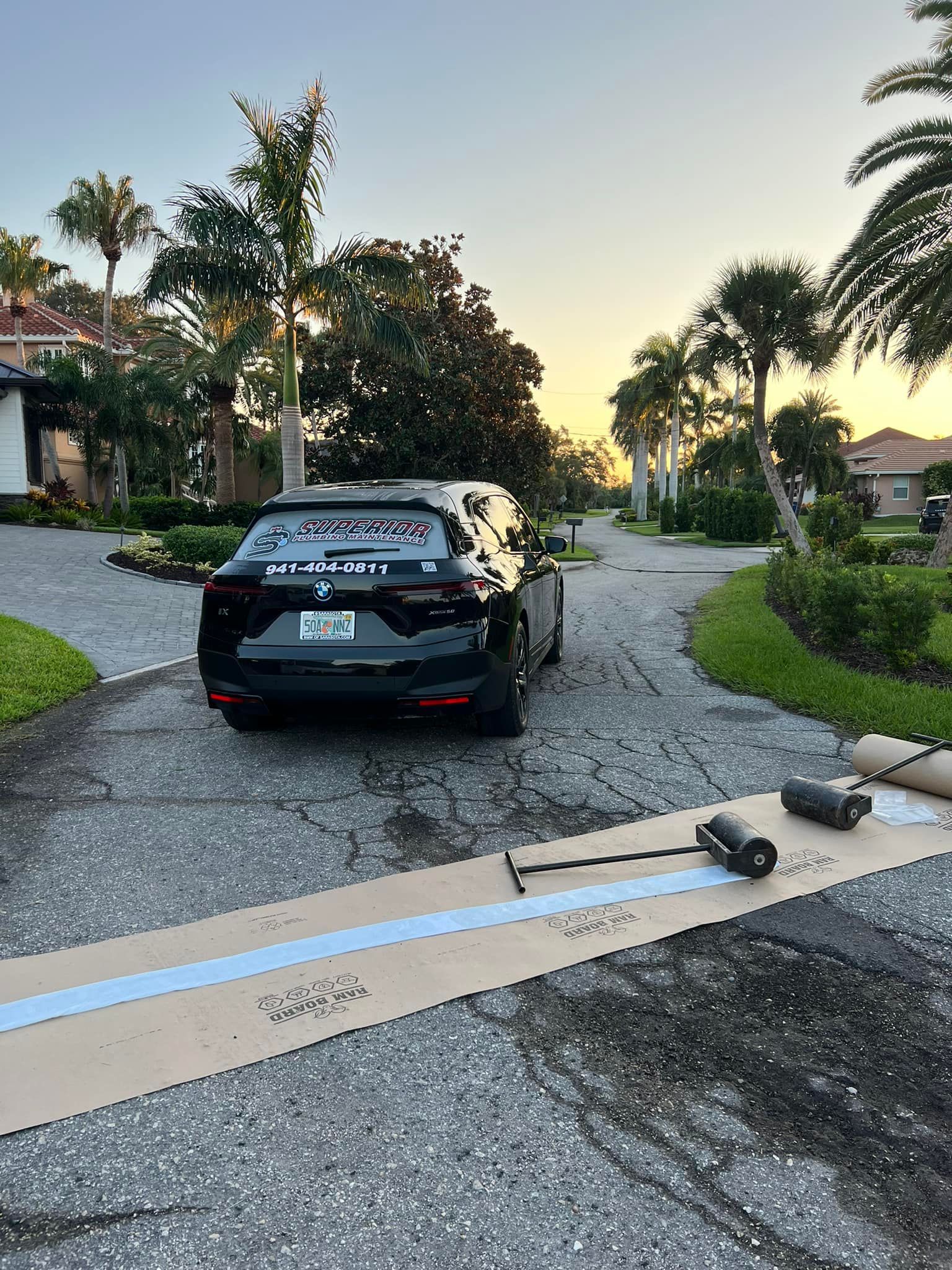 Black SUV parked on a driveway with rolled mats laid out; palm trees and houses in the background.